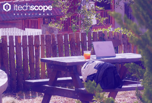 an open laptop on a park bench presumably in a park with an orange drink on the side.